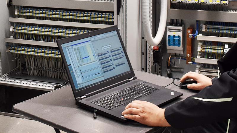Mitarbeiter am Laptop nimmt Schaltschrank in Betrieb